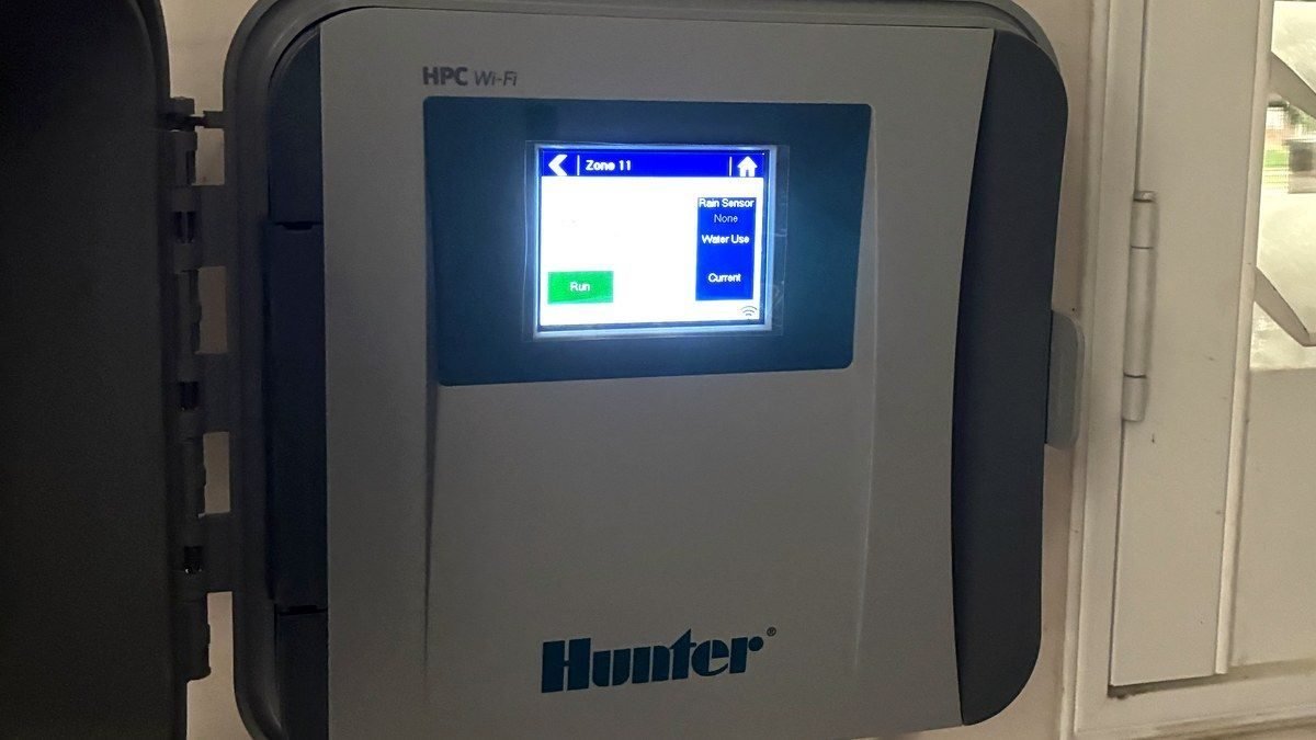 Wall-mounted WiFi sprinkler controller with its door open, showing zone 11 on the screen.